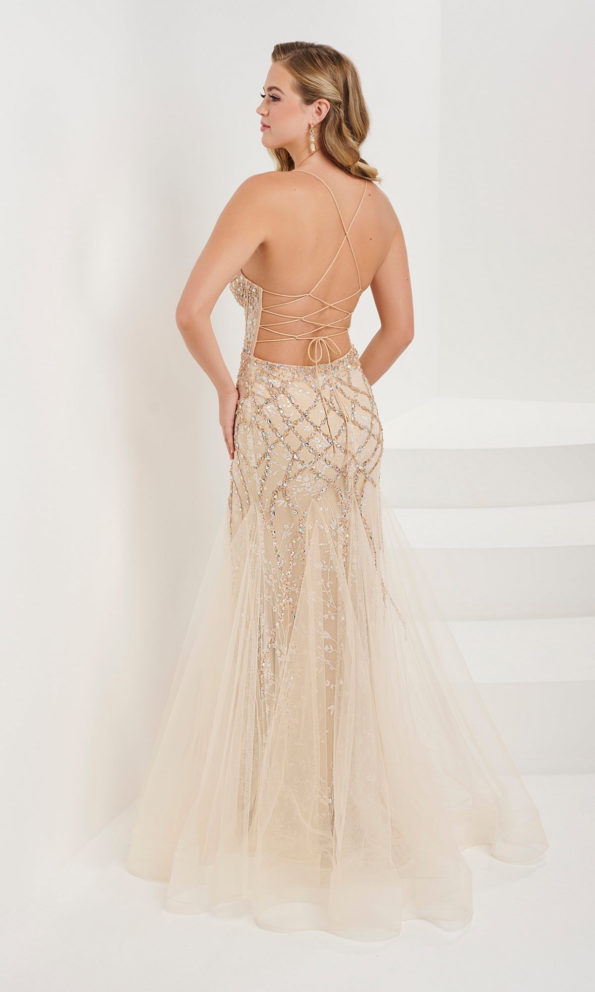 A woman poses with her back to the camera in a white, minimalist setting wearing the Tiffany Beaded Lilac Purple Mermaid Prom Dress 16105, featuring sparkling beadwork and crisscross straps.